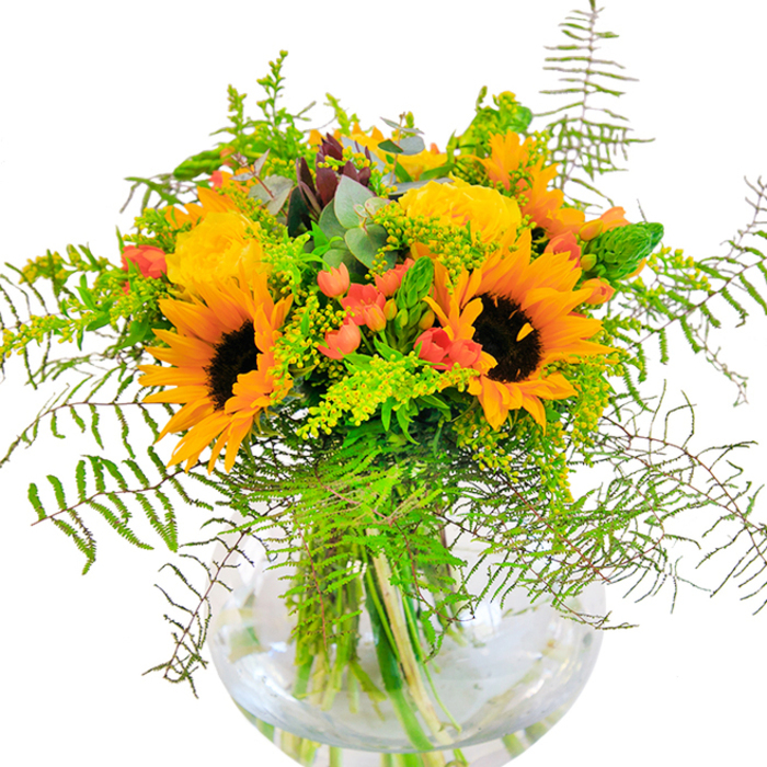 This luxurious floral composition is a sunlit celebration that echoes the changing seasons of West Drayton. Radiant sunflowers form the backbone of the bouquet, their wide petals and deep brown centers capturing the vibrant energy of a mid-summer morning on Green Lane. Alongside, soft yellow garden roses open in tightly layered spirals, exuding elegance and classic beauty. Deep green leaves and air-light vines cascade throughout the display, recalling the lush greenery of the Colne Valley Park. Scarlet hypericum berries, nestled among the foliage, provide sparkling, glossy contrast, while whisps of goldenrod and slender floral spikes soften the edges of the bouquet, lending an almost dance-like movement. Blue-green eucalyptus adds depth with subtle highlights and a faintly herbal aroma. The clear glass globe vase, reminiscent of the timeless vessels displayed in West Drayton's florists, cradles the stems and allows the intricate symmetry of the arrangement to be fully seen. A gentle medley of textures-soft, velvety sunflowers, plump roses, crisp greens-creates a tactile delight. Subtly perfumed, this bouquet captures the atmosphere of sun-warmed fields on a quiet afternoon. Crafted by flowers West Drayton, this arrangement is the perfect centerpiece for any local occasion, gift, or moment where happiness, gratitude, and natural splendour take centre stage.